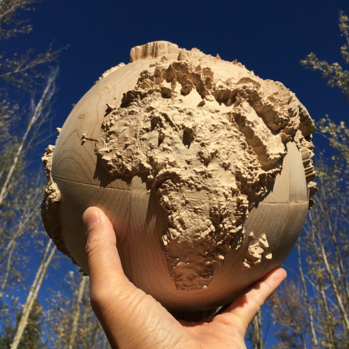 fully three-dimensional wood-carved terrestrial globe held in my hand with blue sky and trees in the background
