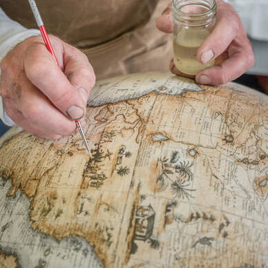 hands of Chris Adams from Lander and May hand-painting a globe