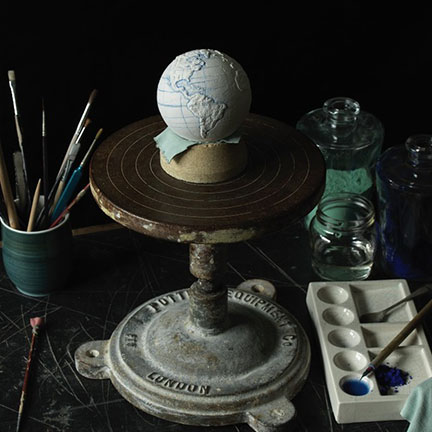 porcelain pocket globe from The Little Globe Co on a metal pottery stand surrounded by paintbrushes and palette